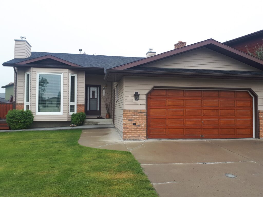 Front view of a beige suburban house with a large wooden garage door and front window.