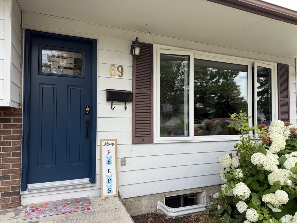 Blue front door beside a large window, house number 69, lantern light, and white hydrangeas in bloom by the entryway.