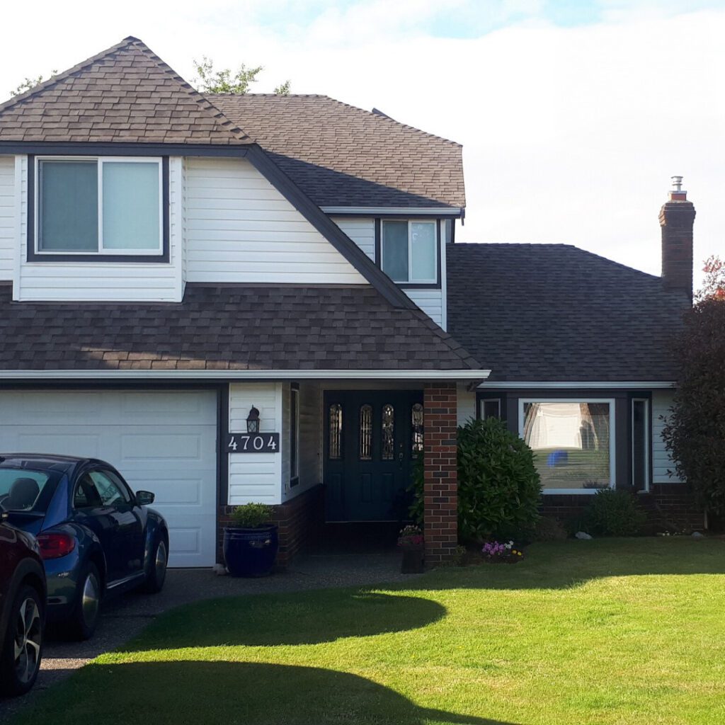 Front view of a two-story house with white siding, dark roof, blue front door, brick column, and attached garage; a blue car is parked in the driveway next to a green lawn and potted plants.